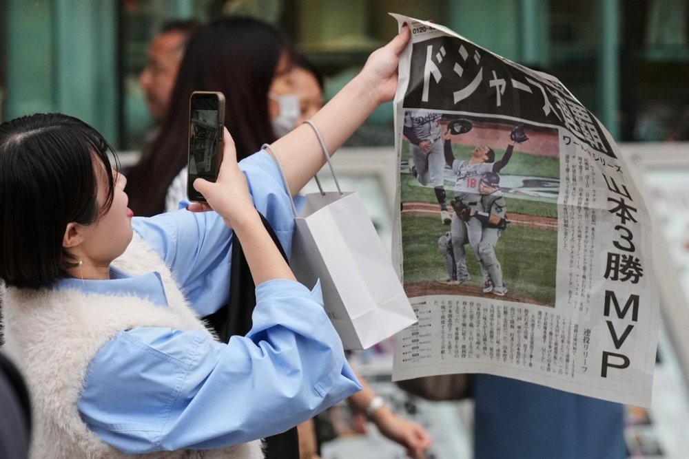 A woman takes a picture of a copy of the extra issue published after the Los Angeles Dodgers won baseball's World Series, as she received it from a Japanese newspaper staffer in Tokyo, Sunday, Nov. 2, 2025. (AP Photo/Hiro Komae)
