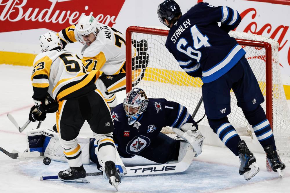 Winnipeg Jets goaltender Eric Comrie (1) saves the shot as Pittsburgh Penguins' Philip Tomasino (53) and Evgeni Malkin (71) attack and Logan Stanley (64) defends during first period NHL action in Winnipeg, Saturday, Nov. 1, 2025. THE CANADIAN PRESS/John Woods
