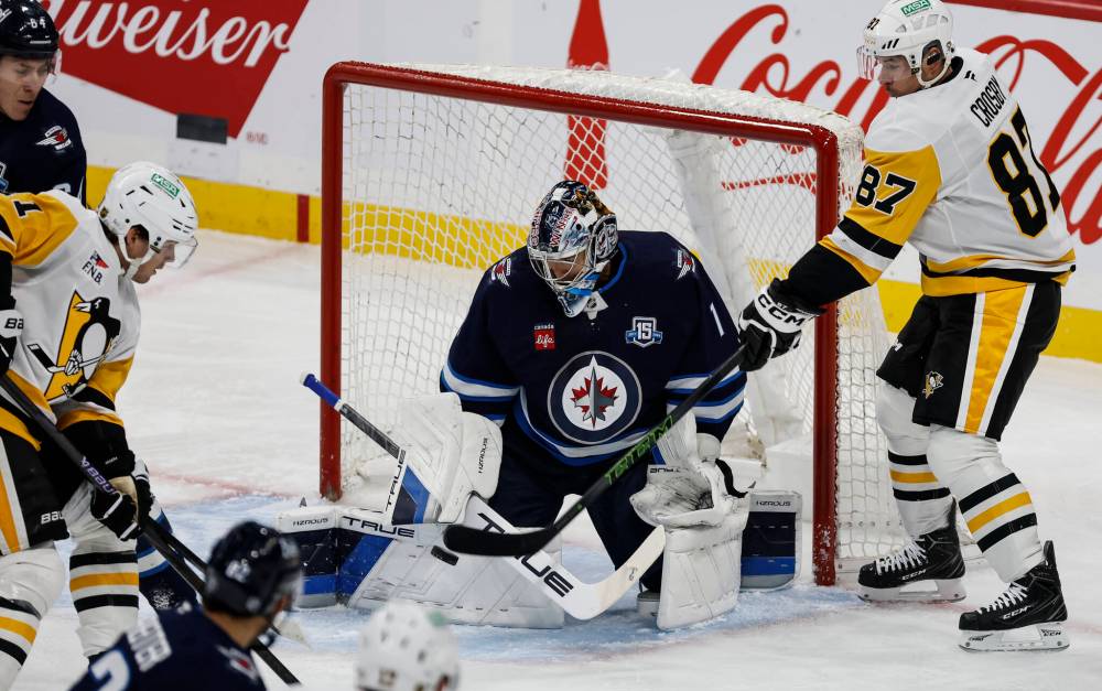 Pittsburgh Penguins' Sidney Crosby (87) tries to tip the puck past Winnipeg Jets goaltender Eric Comrie (1) during first period NHL action in Winnipeg, Saturday, Nov. 1, 2025. THE CANADIAN PRESS/John Woods