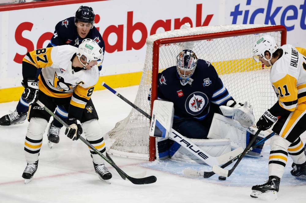 Pittsburgh Penguins' Sidney Crosby (87) makes the pass in front of Winnipeg Jets goaltender Eric Comrie (1) during second period NHL action in Winnipeg, Saturday, Nov. 1, 2025. THE CANADIAN PRESS/John Woods