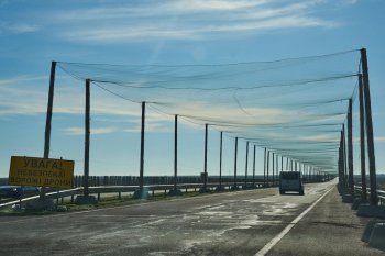 A car drives on a road covered with an anti-FPV-drone net, a road sign reading 