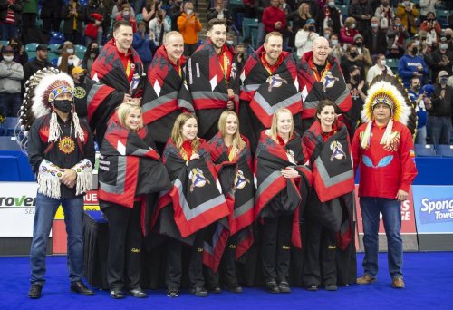 Whitecap Dakota First Nation Chief Darcy Bear, left, and Saskatoon Tribal Council Tribal Chief Mark Arcand, right, pose with members of Team Gushue and Team Jones at the podium after receiving star blankets during the 2021 Canadian Olympic curling trials in Saskatoon on Nov. 28, 2021. THE CANADIAN PRESS/Rick Elvin