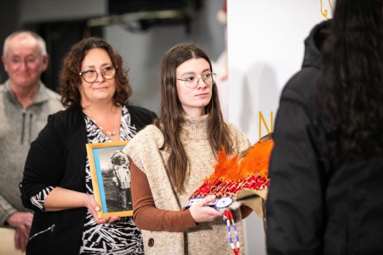 Fort la Reine Museum representative Caitlin Post carries the headdress in the grand entrance procession during a repatriation ceremony at Long Plain First Nation urban reserve in Portage la Prairie on Tuesday, Dec. 16. (Mikaela MacKenzie / Free Press)