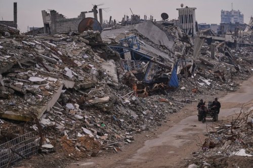 Palestinians pass along a street surrounded by buildings destroyed during Israeli air and ground operations in the Sheikh Radwan neighborhood, in Gaza City, Tuesday, Dec. 30, 2025. (AP Photo/Abdel Kareem Hana)