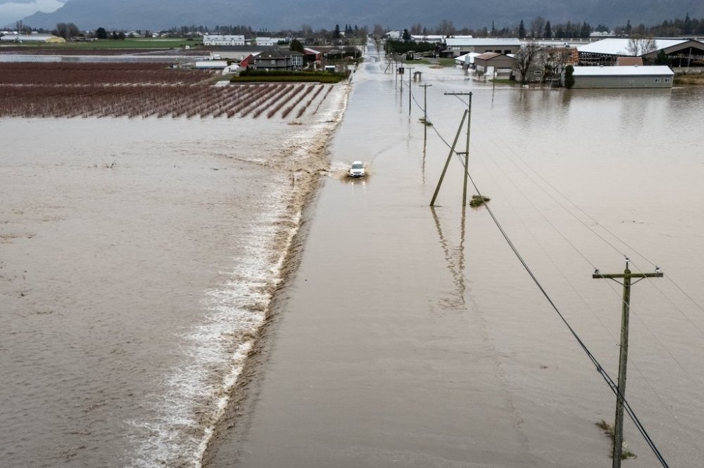 A car crosses a flooded street in Abbotsford B.C., on Thursday, Dec. 11, 2025. THE CANADIAN PRESS/Ethan Cairns