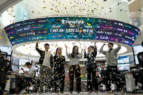 Currency traders celebrate as they work in the office with a screen showing the Korea Composite Stock Price Index (KOSPI), center top, of over 5,000 points at the foreign exchange dealing room of the Hana Bank headquarters in Seoul, South Korea, Thursday, Jan. 22, 2026. (AP Photo/Ahn Young-joon)