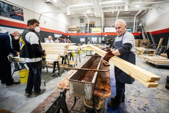 Peter Parys (right) dips wood pieces in a vinegar and steel wool solution (which acts as a stain and bedbug inhibitor) before being assembled into beds, which will be shipped to Pukatawagan this week. (Mikaela MacKenzie / Free Press)