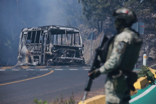 A soldier stands guard by a charred vehicle after it was set on fire, in Cointzio, Michoacan state, Mexico, Sunday, Feb. 22, 2026, following the death of the leader of the Jalisco New Generation Cartel, Nemesio Oseguera, known as 