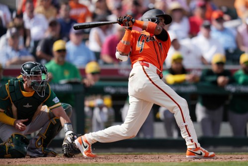 San Francisco Giants' Luis Arraez, right, connects for a run-scoring single as Athletics catcher Austin Wynns, left, looks on during the third inning of a spring training baseball game Monday, Feb. 23, 2026, in Scottsdale, Ariz. (AP Photo/Ross D. Franklin)