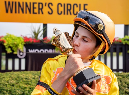 Jockey Pietro Moran kisses the trophy reading 