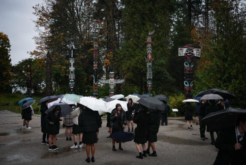High school students from Japan use umbrellas to shield themselves from the rain while stopping to view the totem poles at Stanley Park, in Vancouver, on Saturday, Oct. 19, 2024. THE CANADIAN PRESS/Darryl Dyck