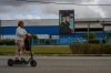 A woman rides an electric scooter past a factory displaying an image depicting the late Cuban leader Fidel Castro, bearing the words 