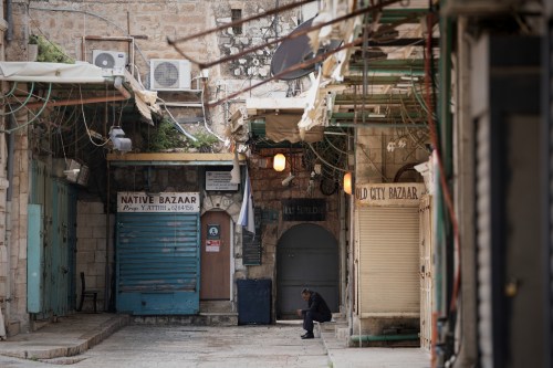 A man sits beside a locked door of the Church of the Holy Sepulchre and shuttered shops in Jerusalem’s Old City, which remains off limits to visitors amid the war with Iran, Friday, March 27, 2026. (AP Photo/Mahmoud Illean)