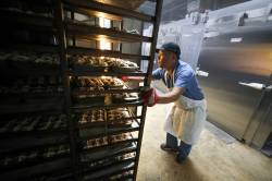 RUTH BONNEVILLE / FREE PRESS
                                49.8 Feature - Hot Cross Buns in the making Photo of lead baker, Julius , moving a full rack of cross buns into the oven Wednesday.