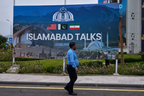 A police officer walks past a billboard regarding U.S. and Iran negotiations, outside a media facilitation center in Islamabad, Pakistan, Saturday, April 11, 2026. (AP Photo/Anjum Naveed)