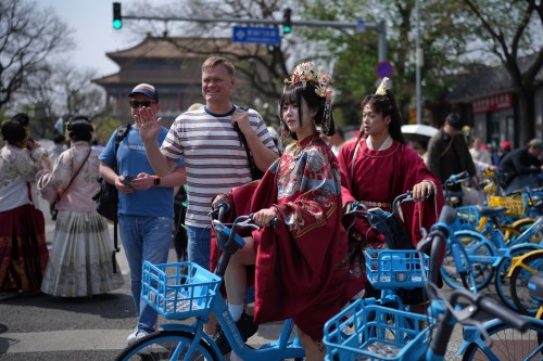 A foreign tourist poses next to a Chinese couple dressed in imperial costumes near the Forbidden City, in Beijing, on Sunday, April 12, 2026. (AP Photo/Andy Wong)