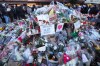 FILE - People stand around floral tributes and candles placed outside the sealed off Le Constellation bar in Crans-Montana, Swiss Alps, Switzerland, on Jan. 3, 2026, where a devastating fire left dead and injured during the New Year's celebrations. (AP Photo/ Antonio Calanni, File)