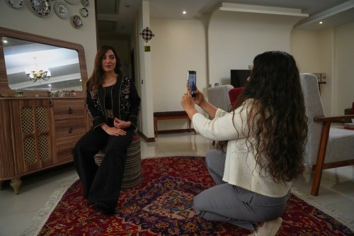 Fashion designer Amen Khademi takes a photo with her cellphone of model Farnaz Ojaghloo wearing a jacket she designed with Persian-inspired motifs at her studio in Tehran, Iran, Thursday, April 23, 2026. (AP Photo/Vahid Salemi)