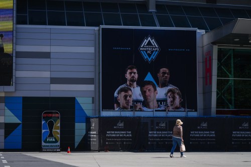 A pedestrian walks past a FIFA World Cup countdown timer and an advertisement with photographs of Vancouver Whitecaps MLS soccer players Thomas Muller, Brian White, Sam Adekugbe, Andres Cubas and Ryan Gauld outside B.C. Place stadium, in Vancouver, on Monday, May 4, 2026. THE CANADIAN PRESS/Darryl Dyck