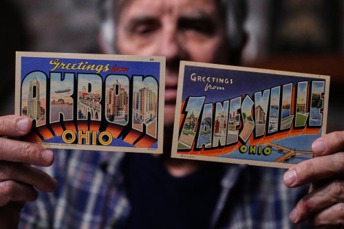 Postcard collector Peter Meggison, holds up two examples of large letter postcards from places across America going from A to Z, Akron to Zanesville, Monday, May 11, 2026, in Westport, Mass. (AP Photo/Charles Krupa)