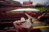Cincinnati Reds fan Robert Plescher, foreground, from Texas, covers his cowboy hat with a rain poncho hood in the stands during a rain delay of a baseball game between the Reds and the St. Louis Cardinals just before it was postponed in Cincinnati, Sunday, May 24, 2026. (AP Photo/Carolyn Kaster)