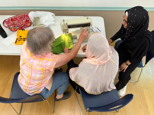 This photo provided by Religion News Service shows Maureen Kurtz, left, working with interpreter Sama Qazikhani, right, to instruct a participant in the Stitching for Hope sewing circle at Eno River Unitarian Universalist Fellowship, Wednesday, May 20, 2026, in Durham, N.C. (RNS photo/Yonat Shimron)