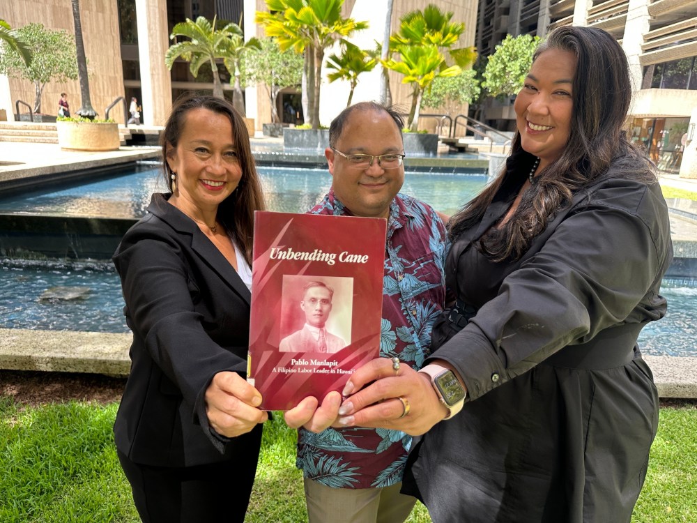 Attorneys Becky Gardner, left, Daniel Padilla, center, and Kainani Collins Alvarez pose with a book about Filipino labor leader Pablo Manlapit on Wednesday, May 27, 2026, in Honolulu. (AP Photo/Jennifer Sinco Kelleher)