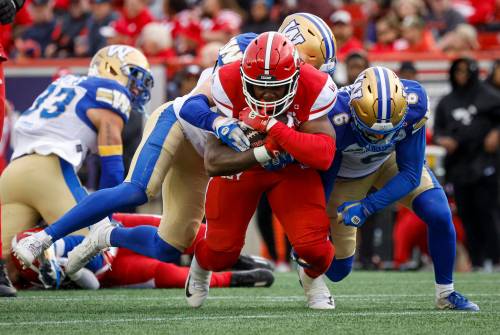 Jeff McIntosh / THE CANADIAN PRESS
                                Blue Bombers&rsquo; Redha Kramdi, right, and Evan Holm, centre, tackle Stampeders running back Dedrick Mills during the first half in Calgary, Friday.