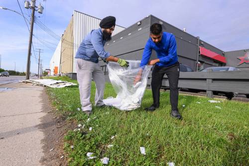 Gurmeet Singh Kharoud (left) and Karanveer Dhanoa (right) clean up debris scattered along St. James Street between Wellington and Saskatchewan avenues Wednesday morning after a large portion of their building lost its siding due to Tuesday night&rsquo;s storm. (Mike Sudoma/Free Press)