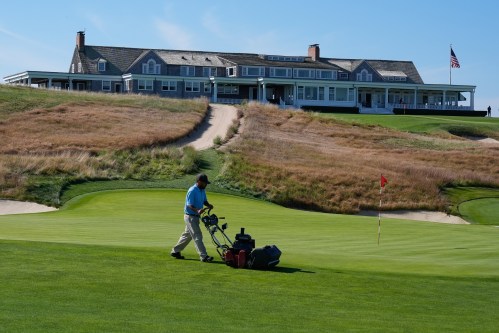 FILE - A man works on the 18th green in front of the clubhouse at Shinnecock Hills Golf Club in Southampton, N.Y., Monday, Sept. 15, 2025. (AP Photo/Seth Wenig, File
