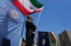 A woman waves an Iranian flag during a pro-government campaign as a portrait of the slain Supreme Leader Ayatollah Ali Khamenei, who was killed in U.S. and Israeli strikes on Feb. 28, is displayed at right, in downtown Tehran, Iran, Monday, June 15, 2026. (AP Photo/Vahid Salemi)