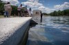 Visitors watch as a National Park Service employee uses a vacuum to clean the Lincoln Memorial Reflecting Pool near a missing section of blue coating, Friday, June 19, 2026, in Washington. (AP Photo/Mark Schiefelbein)