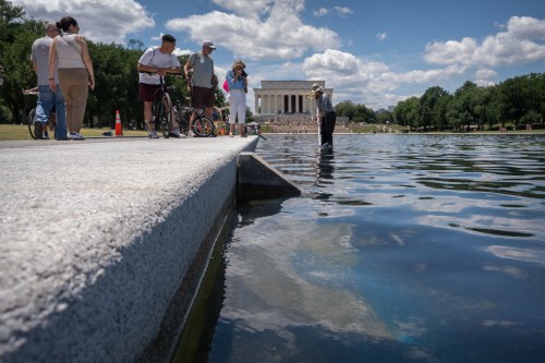 Visitors watch as a National Park Service employee uses a vacuum to clean the Lincoln Memorial Reflecting Pool near a missing section of blue coating, Friday, June 19, 2026, in Washington. (AP Photo/Mark Schiefelbein)