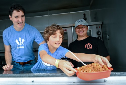 Prime Minister Justin Trudeau and son Hadrien serve a poutine as they visit a poutine festival in Chateauguay, Que., Sunday, June 23, 2024. THE CANADIAN PRESS/Graham Hughes