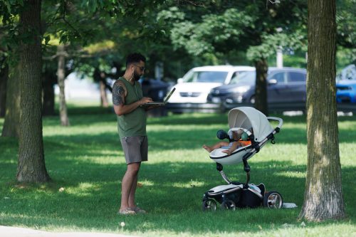 A man is seen on his laptop in the park while a baby naps, in the park on the Toronto waterfront, Thursday July 6, 2023. THE CANADIAN PRESS/Cole Burston