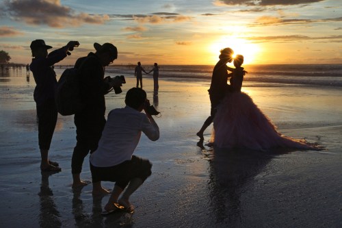 FILE- In this Jan. 18, 2017, file photo, photographers take photos of a tourist couple's wedding at the famous Kuta beach during sunset in Bali, Indonesia. (AP Photo/Firdia Lisnawati, File)