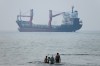 A group of people stands in shallow water as a cargo ship appears anchored in the Strait of Hormuz off Bandar Abbas, Iran, Tuesday, June 30, 2026. (Amirhosein Khorgooi/ISNA via AP)