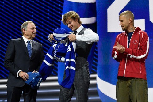 Gavin McKenna, centre, puts on a jersey after being drafted by the Toronto Maple Leafs as NHL Commissioner Gary Bettman, left, and singer Justin Bieber look on during the NHL hockey draft Friday, June 26, 2026, in Buffalo, N.Y. (AP Photo/Adrian Kraus)