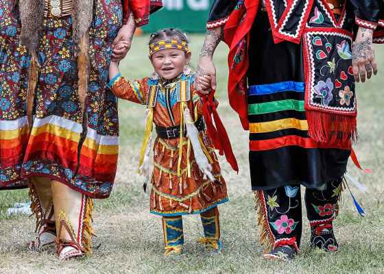 Nahanni walks hand-in-hand with her aunt Cayla Houle and mother Destiny Houle as they wait to participate in the grand entrance of the powwow at Anishinaabe Days on Sunday. (John Woods / Free Press)