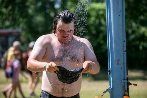 BROOK JONES / FREE PRESS
                                Folk Fest attendee Miles Bruns, 32, from Madison, Wis., tries to keep cool on an extremily hot summer day by filling up his bucket hat with water from an outdoor shower at Birds Hill Provincial Park, Sunday.