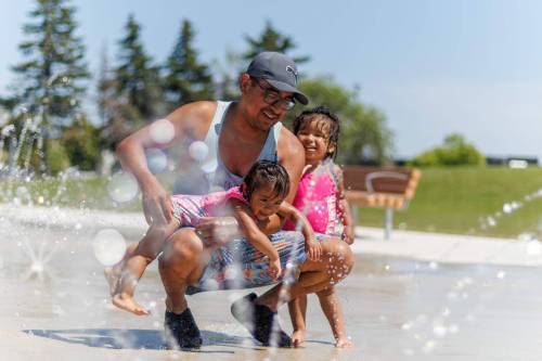 MIKE DEAL / FREE PRESS Joannes Mendivil and his two daughters, Pia, 2, and Paula, 1, take advantage of the cool water at the Maples Spray Pad Monday afternoon. Reporter: Tiago Resko 260713 - Monday, July 13, 2026.