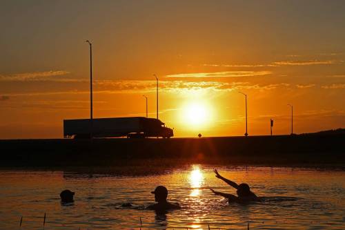 Three young men swim in the floodwaters of the swollen Assiniboine River along Grand Valley Road at the Trans-Canada Highway at sunset on Monday evening. Brandonites and area residents gathered at the road to fish, wade, swim and watch carp swim across the roads and through the flooded fields. (Tim Smith/The Brandon Sun)
