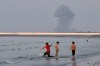 Three boys play in the shallow waters of the Strait of Hormuz, as a plume of smoke rises from an explosion in the background, off Bandar Abbas, Iran, Monday, July 13, 2026. (Razieh Poudat/ISNA via AP)