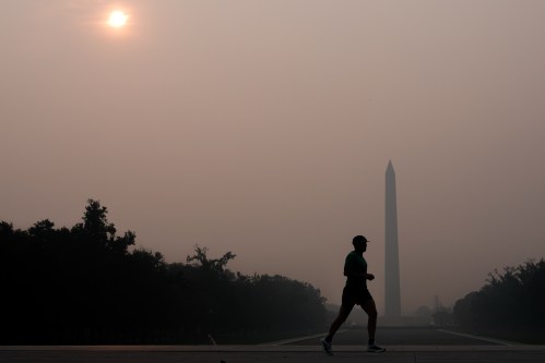 The sun is obscured by wildfire smoke as a person runs in front of the Washington Monument and Lincoln Memorial Reflecting Pool, Friday, July 17, 2026, on the National Mall in Washington. (AP Photo/Julia Demaree Nikhinson)