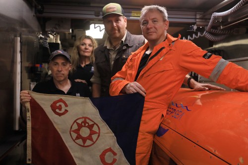This undated photo provided by the Discovery Channel Tuesday, July 21, 2026, shows, from left, Air/Sea Heritage Foundation (ASHF) President Russ Matthews, ASHF Director Idee Matthews-Montijo, Expedition Unknown's Josh Gates and Deep Sea Visoin President of Operations Craig Wallace inside an AUV hangar with an Explorers Club flag. (Discovery Channel via AP)