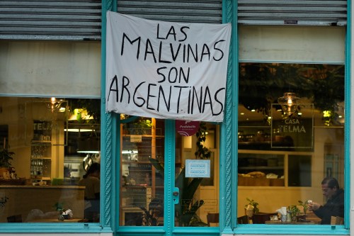 A man sits at a restaurant displaying a banner reading 