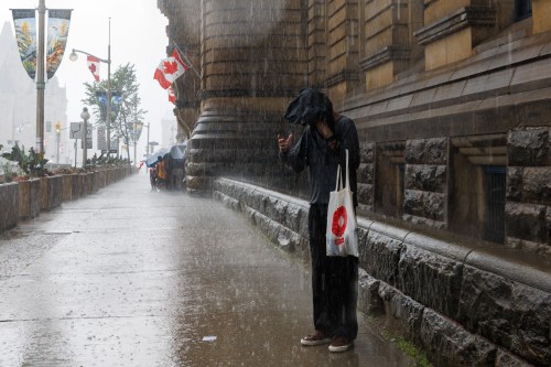 A person tries to take cover as heavy rains falls in Ottawa, on Wednesday, July 1, 2026. THE CANADIAN PRESS/Keito Newman