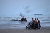 Young men ride motorcycles along the shore as a tractor pulls equipment from the water and commercial vessels appear anchored in the Strait of Hormuz off Bandar Abbas, Iran, Monday, July 27, 2026. (Razieh Poudat/ISNA via AP)
