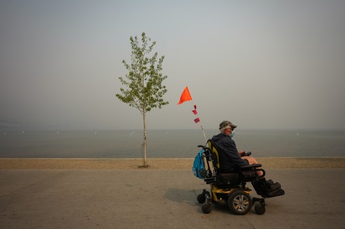 A man using a wheelchair wears a mask due to poor air quality as smoke from the Bald Range wildfire envelops Okanagan Lake, in Penticton, B.C., on Sunday, Aug. 9, 2026. THE CANADIAN PRESS/Darryl Dyck