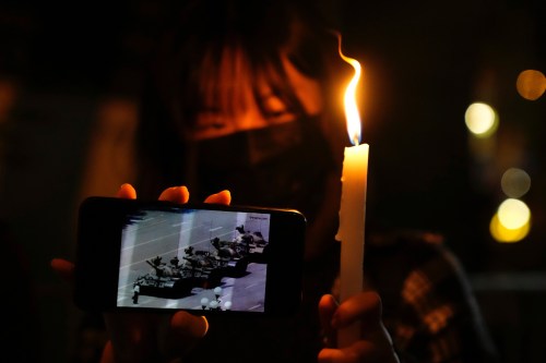 FILE -A woman holds up a candle and an image of a man facing off tanks to mark the anniversary of the military crackdown on a pro-democracy student movement in Beijing, during a light candle vigil outside Victoria Park in Hong Kong, Friday, June 4, 2021. (AP Photo/Kin Cheung, File, File)